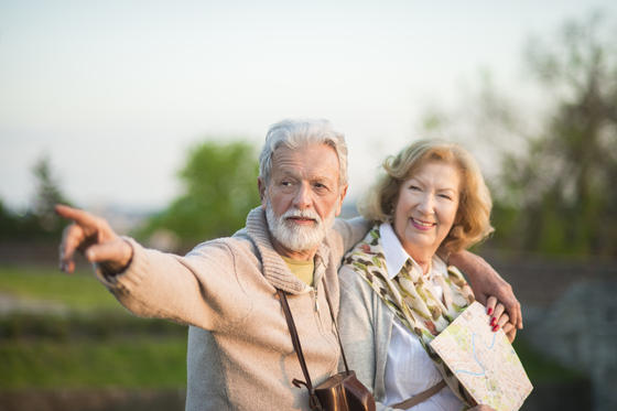 Älteres Paar mit Kamera und Landkarte. Er zeigt ihr etwas in der Ferne.